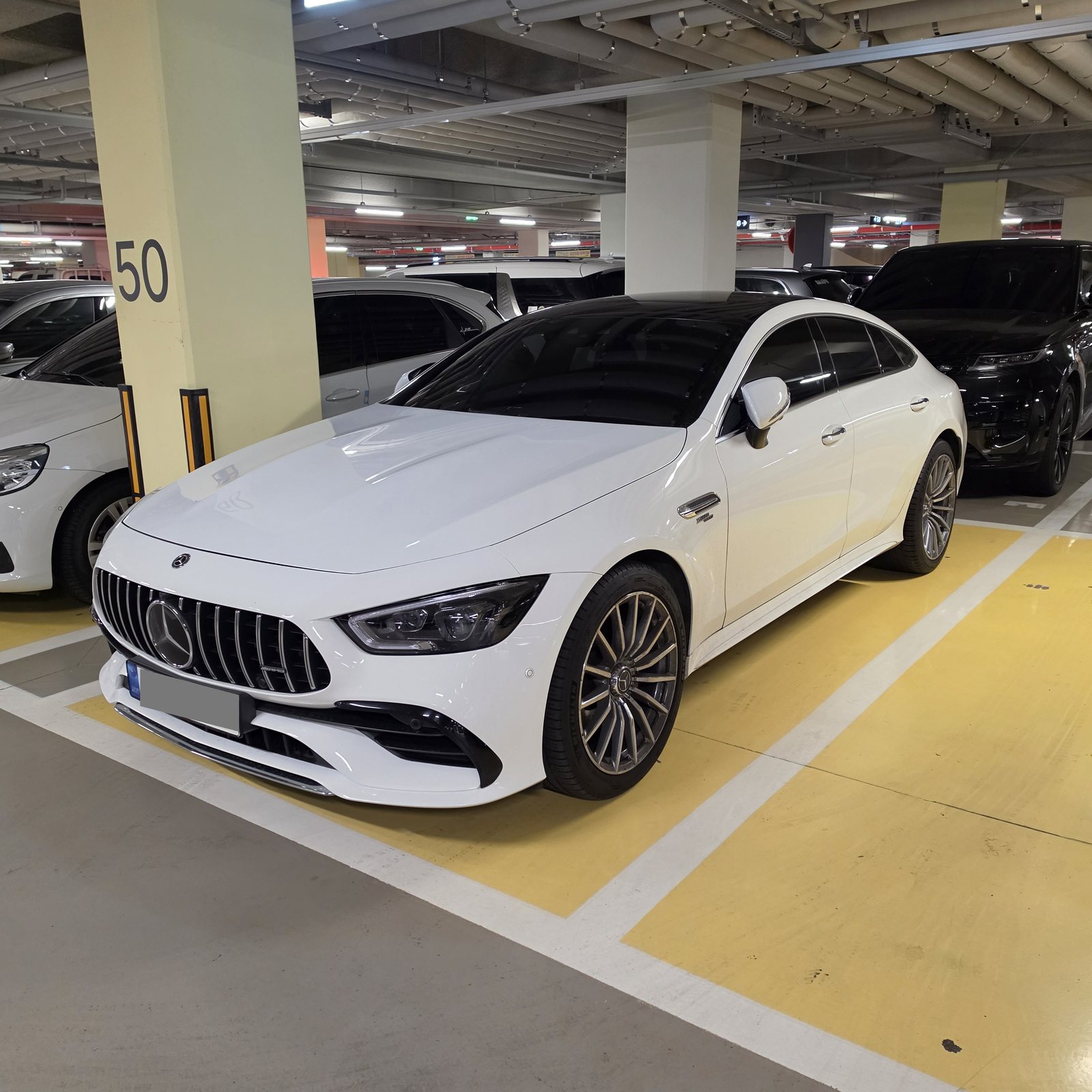 AMG GT43 좌측 전면 3/4 각도. 프론트 스플리터가 범퍼 아래로 내려와 있다. 번호판은 가렸다.